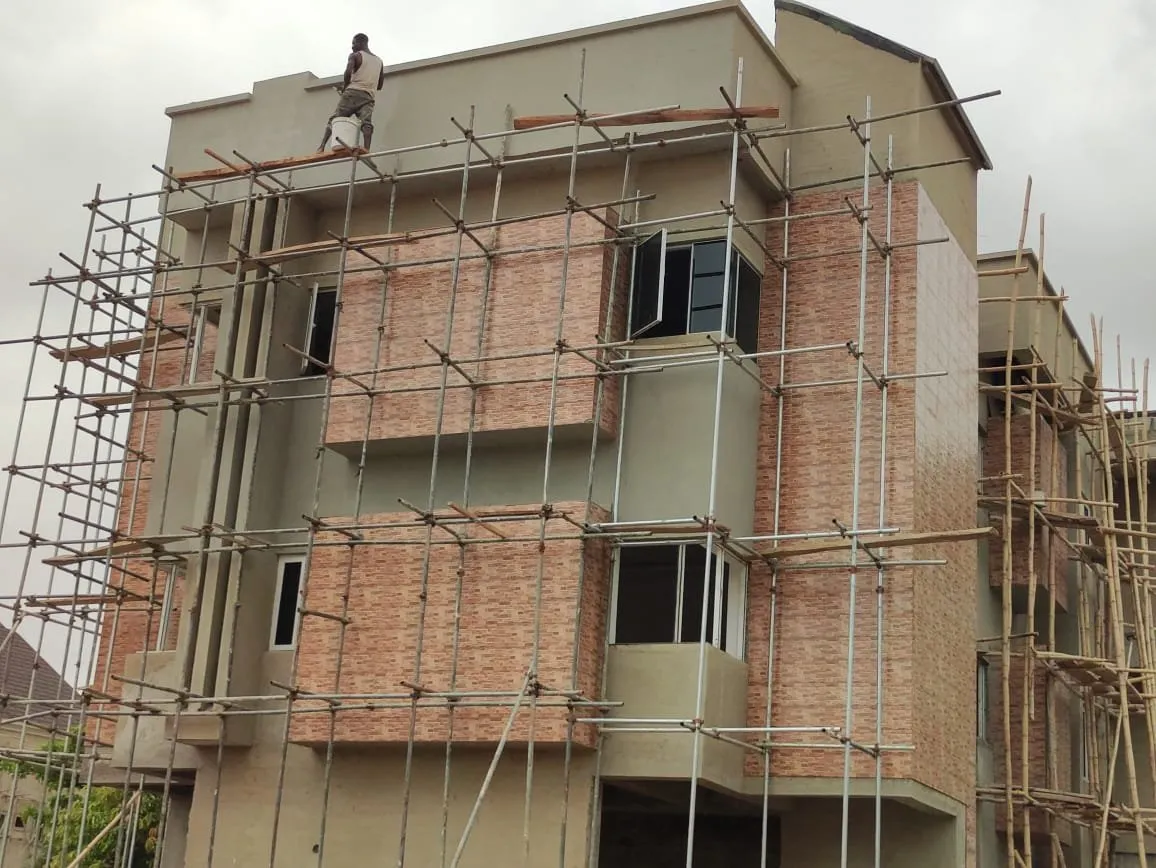 Residential block in scaffolding with brick-red cladding panels, a worker on the roof