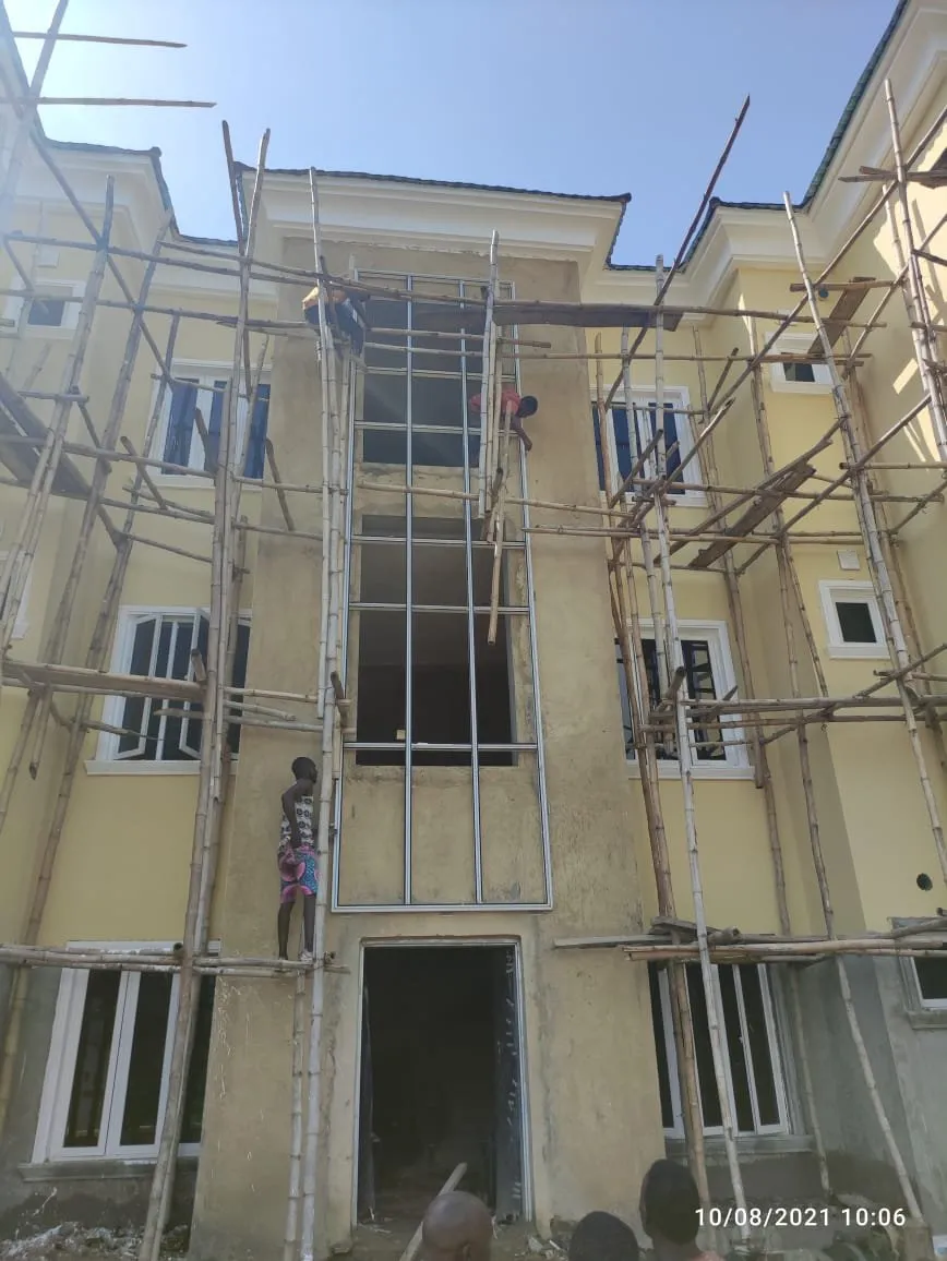 Three-storey residential block in scaffolding, rendered and painted, a worker on a ladder at the entrance