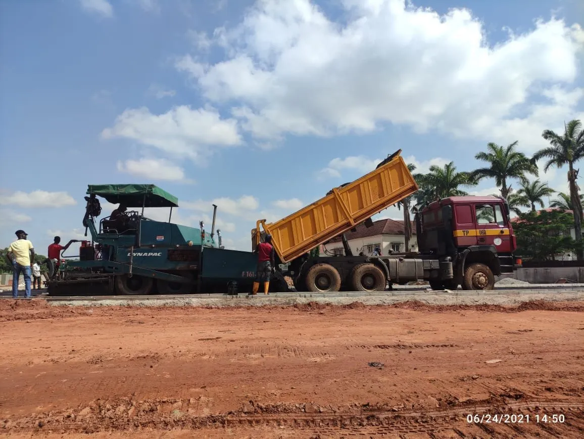 Asphalt paver and tipper truck on a new road with red laterite shoulders
