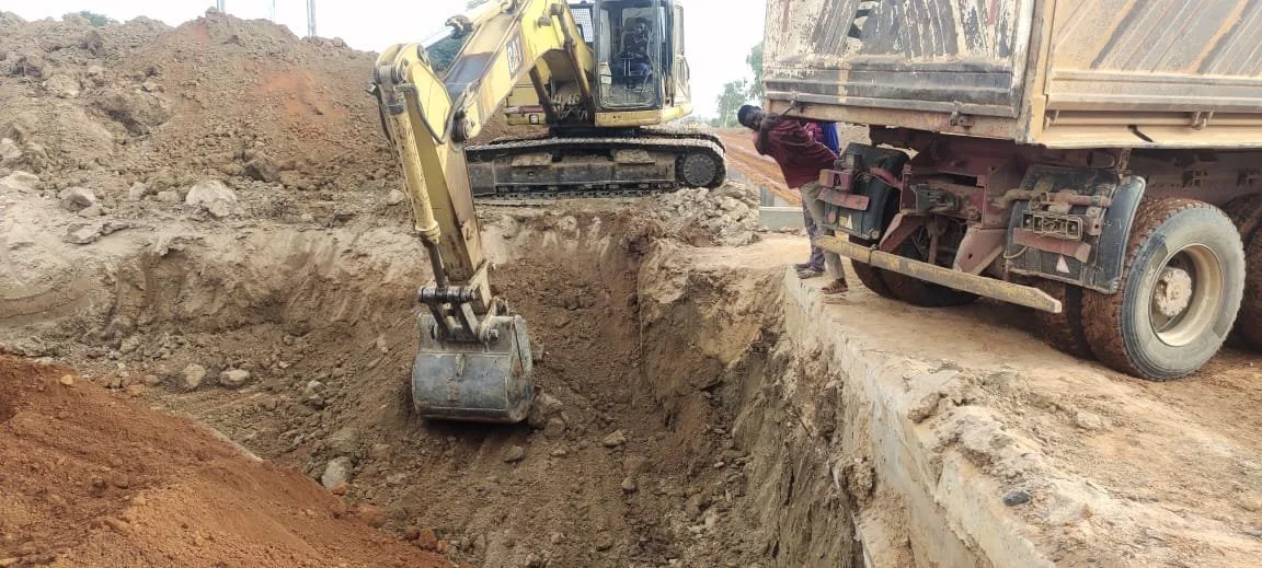 Excavator digging a drain trench beside a tipper truck