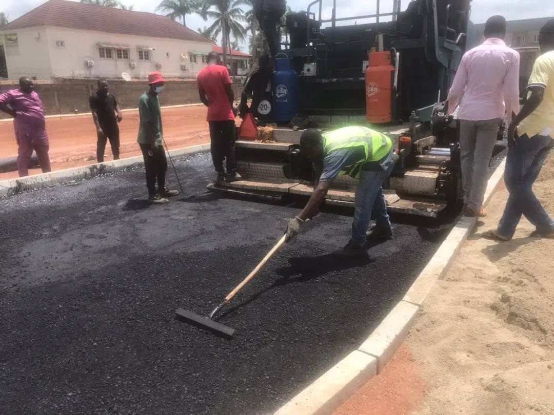Workers raking fresh asphalt behind the paver beside a new kerb