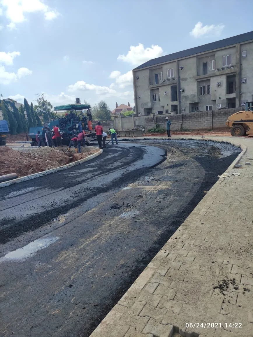 Freshly laid asphalt bend with an interlocking-paved walkway, paving crew in the distance