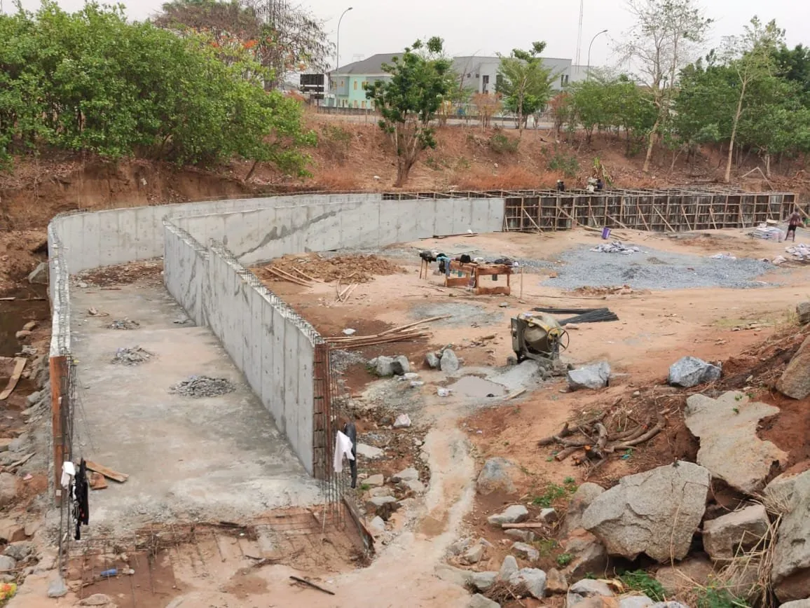 Concrete retaining walls of a channel under construction, houses in the background