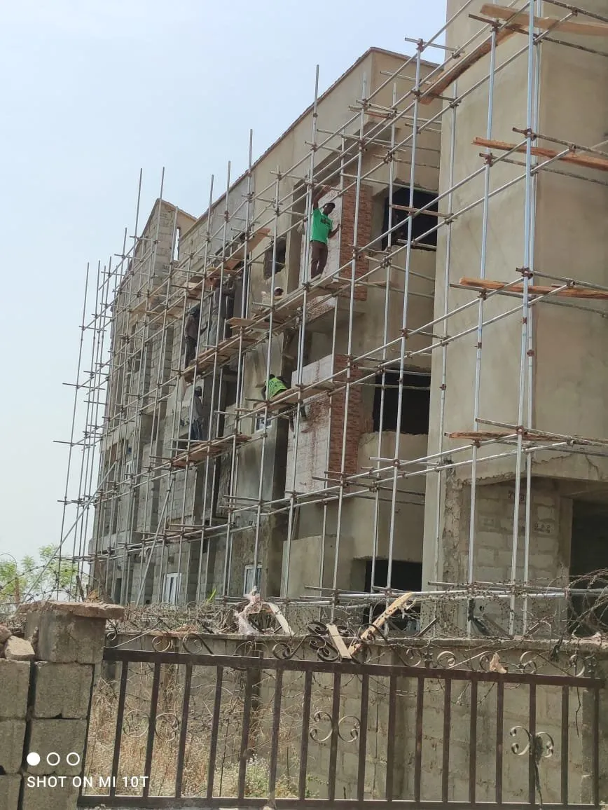 The block seen over the site fence, workers on the scaffolding